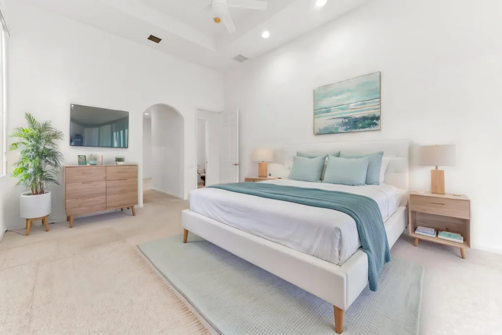20261007212914231431000000-o - Lake Worth Homes - Lake Worth Homes Bright modern bedroom with a king bed, teal pillows and throw, and sea-toned artwork above the headboard, flanked by wooden nightstands and lamps.