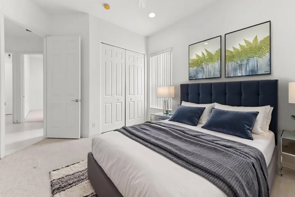 20261007221732534368000000-o - Lake Worth Homes - Lake Worth Homes Bright modern bedroom with a navy tufted headboard, white bedding, and a gray throw beneath two fern art prints above the bed.