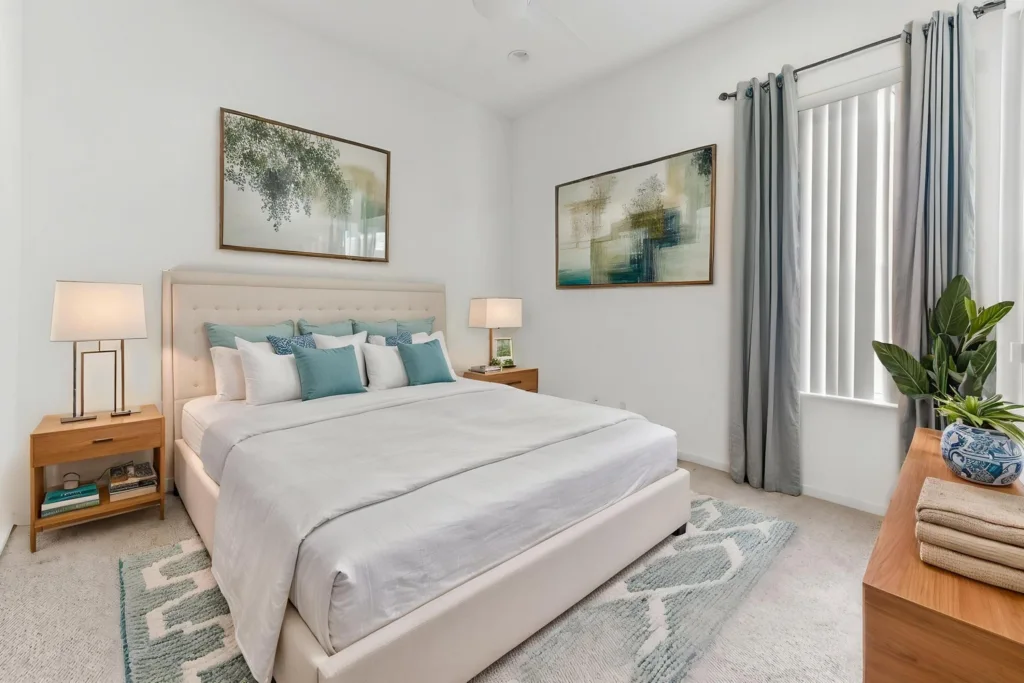 20261007212908156933000000-o - Lake Worth Homes - Lake Worth Homes Bright bedroom with a tufted beige bed, white bedding, and teal cushions, flanked by wooden nightstands and lamps.