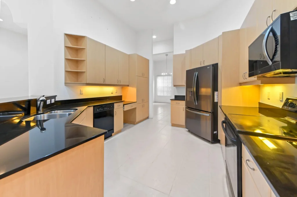20261007212446173096000000-o - Lake Worth Homes - Lake Worth Homes Bright modern galley kitchen with light wood cabinets, black granite counters, and stainless-steel appliances under warm under-cabinet lighting