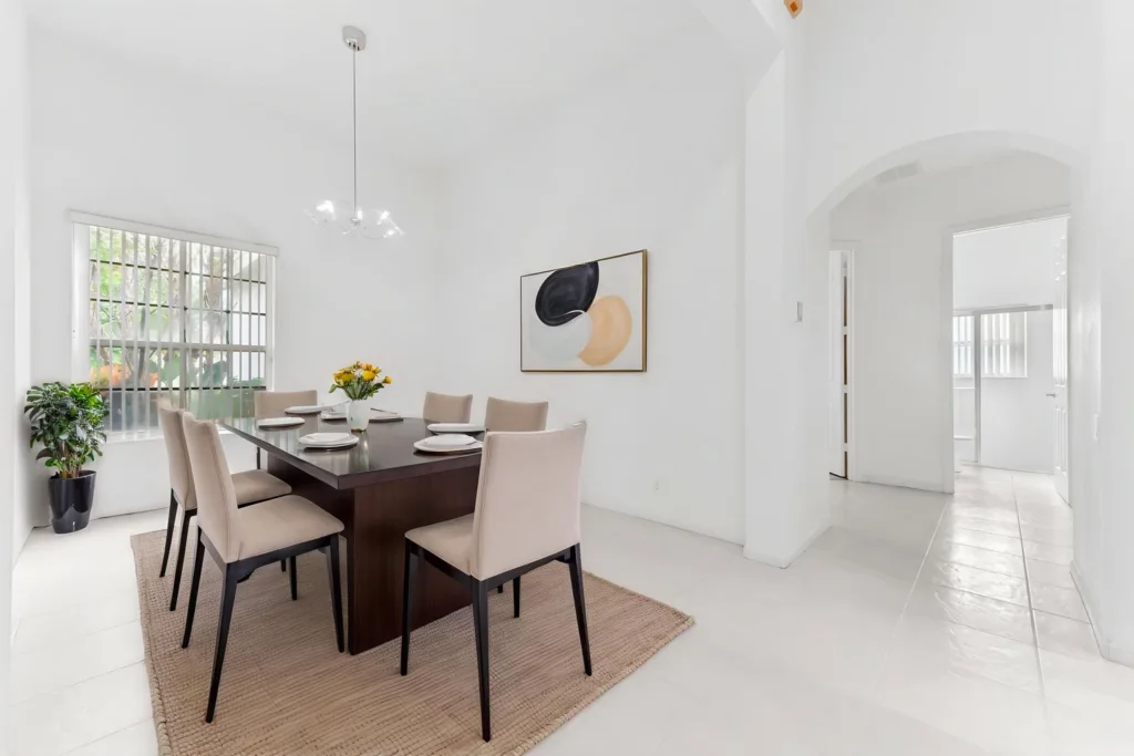 20261007212917675676000000-o - Lake Worth Homes - Lake Worth Homes Ground-floor dining area with a dark wooden table set for six, beige chairs, and a vase of yellow flowers on a light rug.