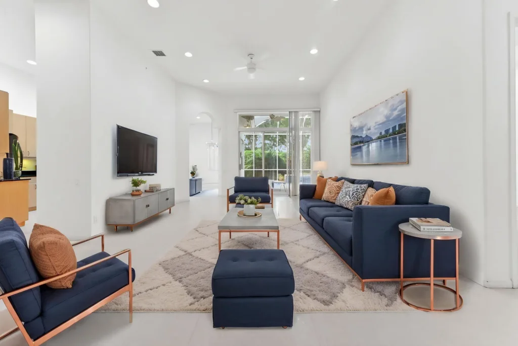 20261007221728486067000000-o - Lake Worth Homes - Lake Worth Homes Modern living room with navy sofa and chairs, copper accents, and a wall-mounted TV across a light rug.