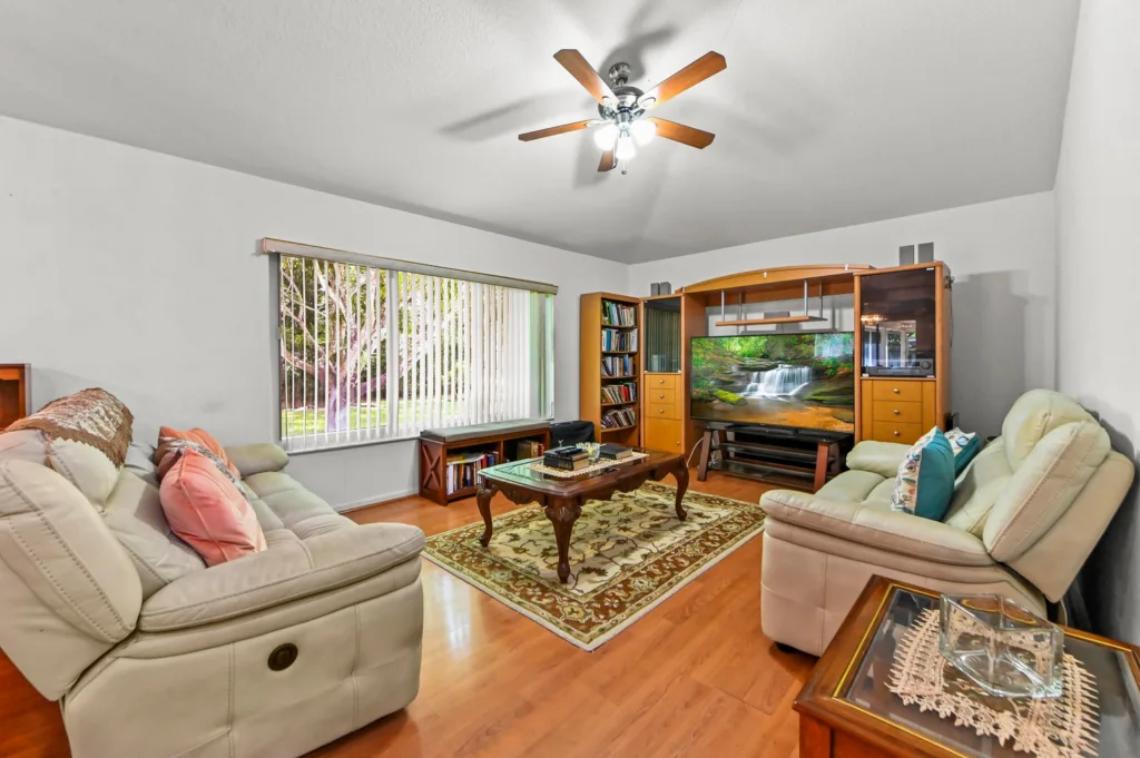 20261006193436975768000000-o - Lake Worth Homes - Lake Worth Homes Cozy living room with beige leather sofas, a glass coffee table, and a large wooden entertainment wall housing a TV showing a nature scene on a rug-framed setup.