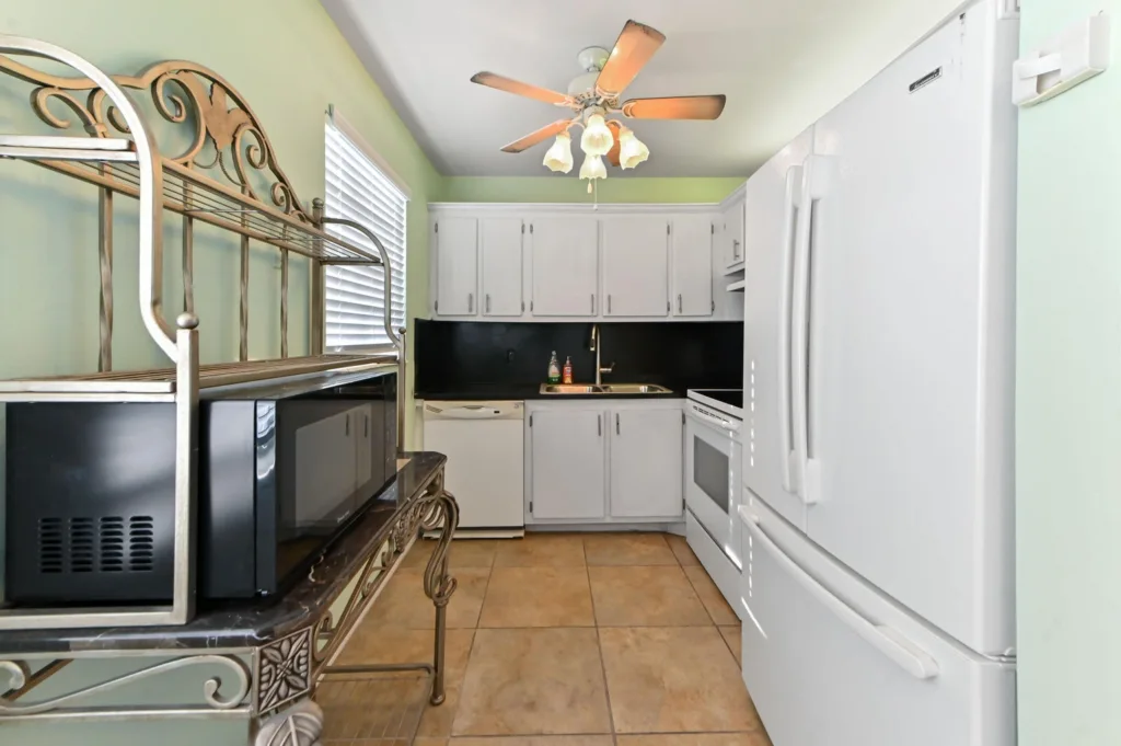 Compact kitchen with white cabinets, beige tile floor, black backsplash, and a large white refrigerator.