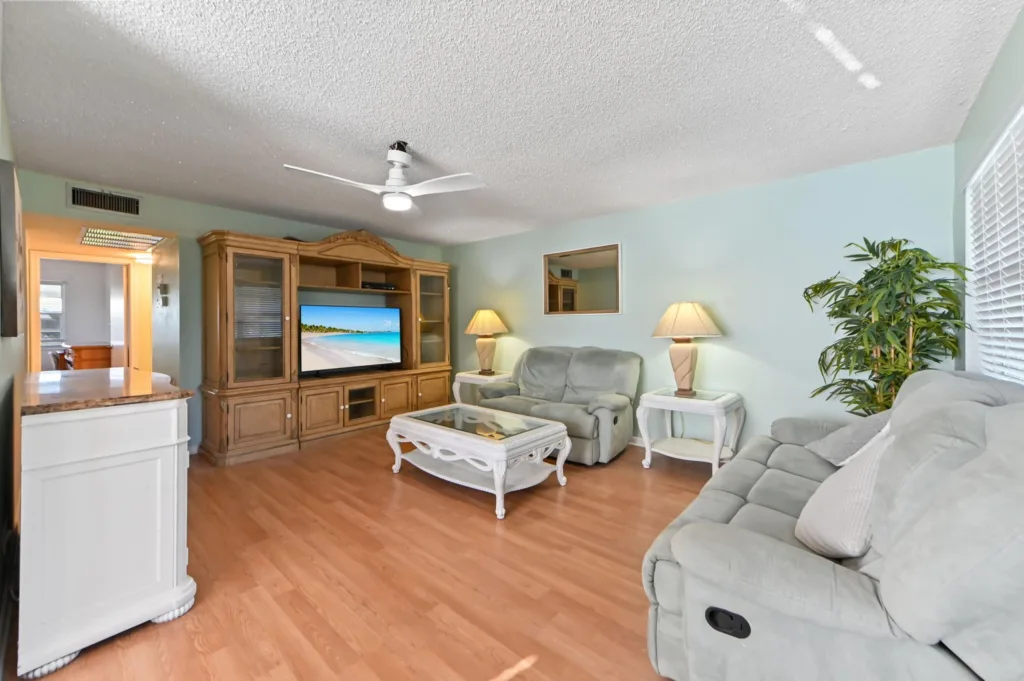Living room with teal walls, beige sofa set, glass coffee table, and a wooden entertainment center with a TV showing a beach scene.