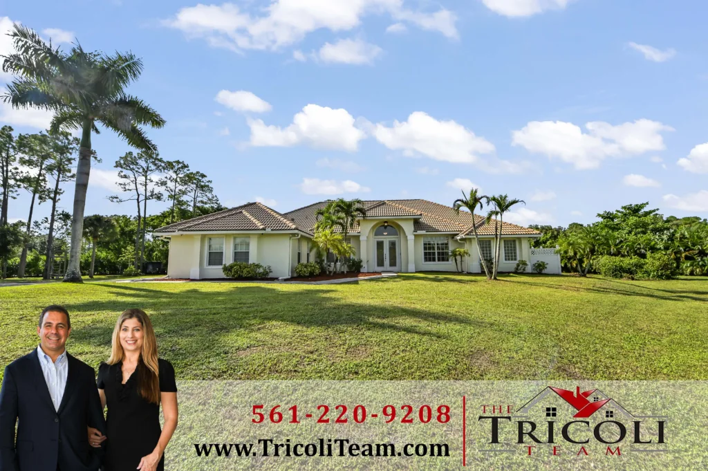 Front yard view of a single-story beige house with a tiled roof and palm trees; a real estate banner with the Tricoli Team branding is in the foreground (bottom).