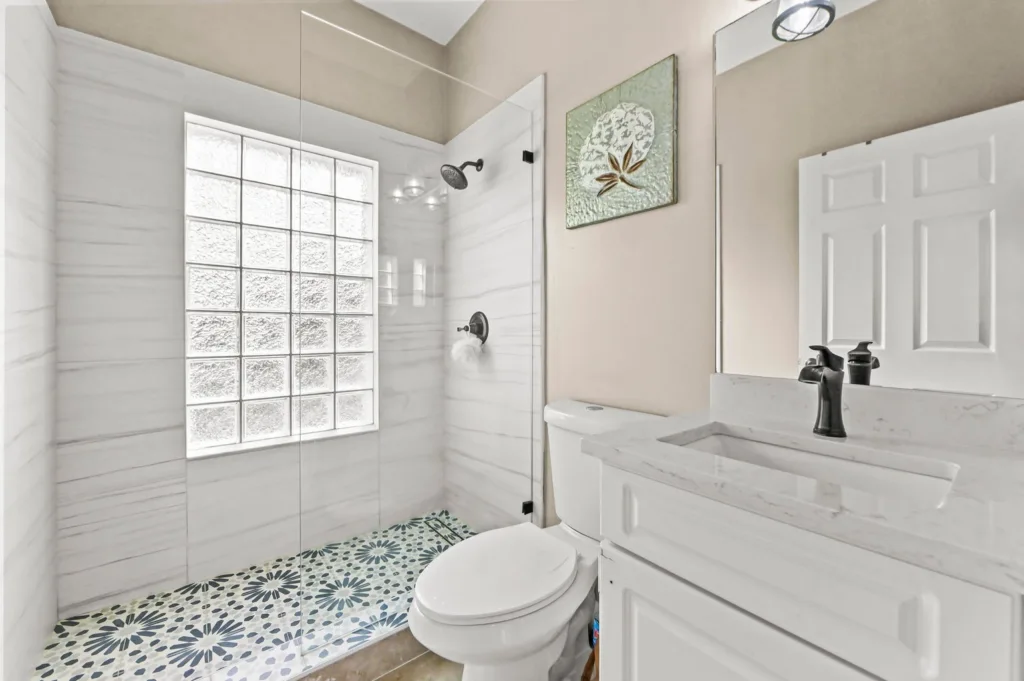 Modern bathroom with glass shower enclosure, white marble walls, and a patterned blue-green tiled floor