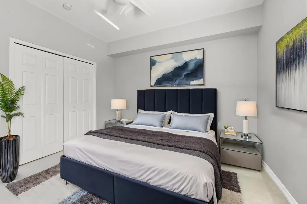 Modern bedroom with a navy headboard, glass nightstands, and abstract blue wall art above the bed.