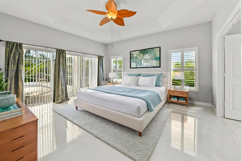 Bright modern bedroom with a white upholstered bed, gray walls, and large glass sliding doors to a balcony.