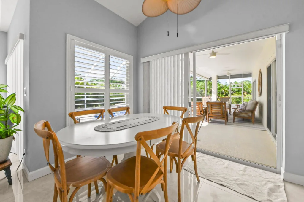 Bright dining area with a white round table and wooden chairs, opening to a sunny patio through a sliding glass door.