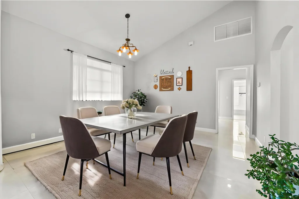 Modern dining room with a rectangular table and eight upholstered chairs, gray walls, and a chandelier above the table