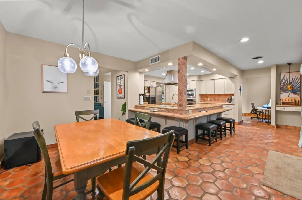 Open-concept kitchen and dining area with a wooden table, dark chairs, and a tiled island in warm earth tones.