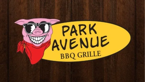 Logo for Park Avenue BBQ Grille featuring a smiling pink pig wearing sunglasses and a red bandana against a wood background.