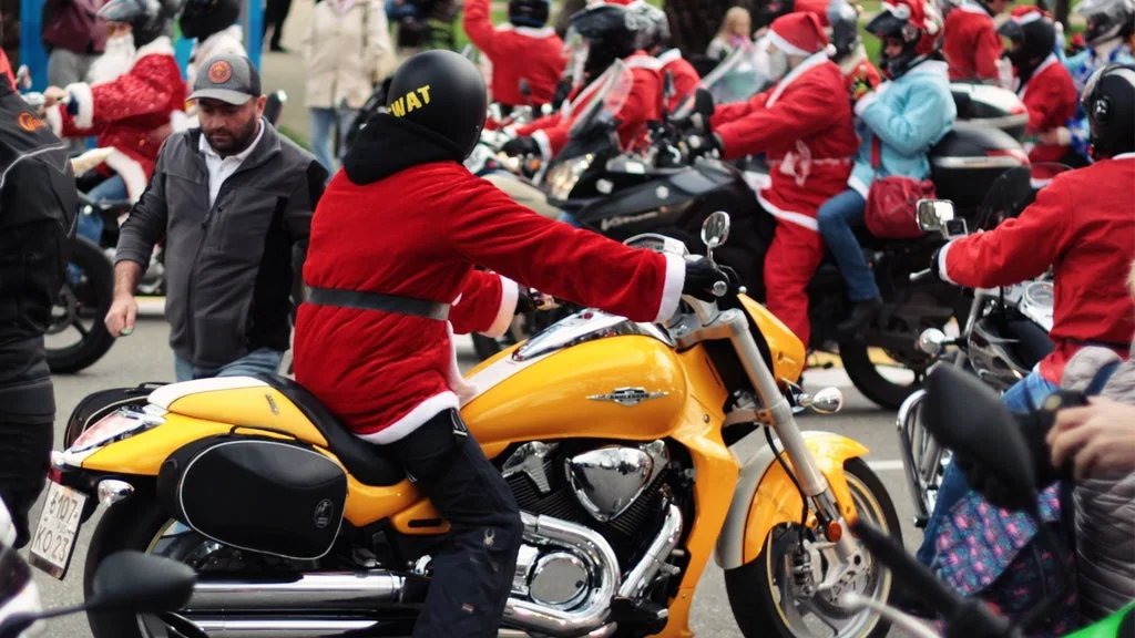Person in a red Santa suit riding a yellow motorcycle in a crowded parade of Santa outfits on bikes.