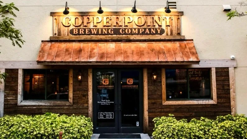 Front view of Copperpoint Brewing Company storefront with a wooden facade, copper awning, and greenery in front.