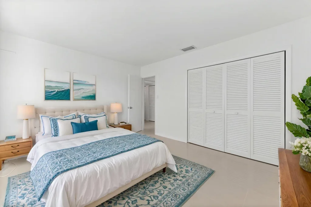 Bright white bedroom with a king bed, blue accents, two nightstands, and a large white closet with louvered doors on the right.