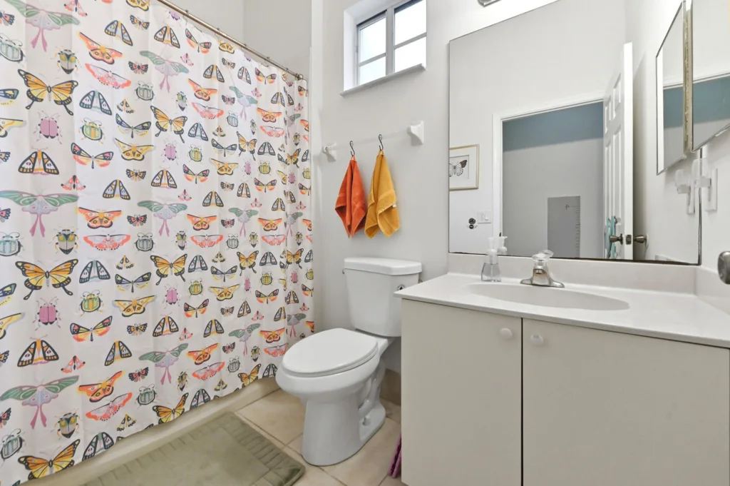 Bright bathroom with a butterfly-pattern shower curtain, white toilet, and white vanity with sink.