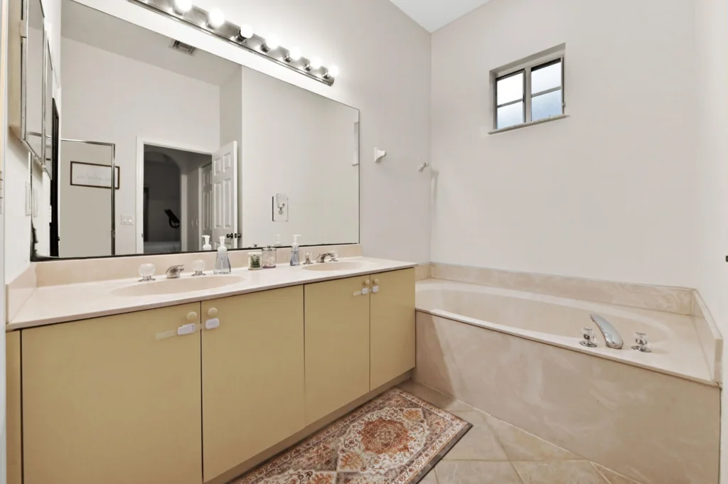 Bathroom with a long beige vanity, large mirror, and row of lights producing a bright reflection.