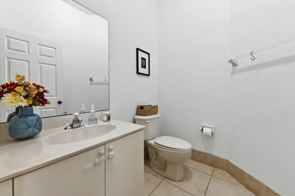 Bathroom sink area with vase of colorful flowers, soap dispenser, and mirror above a beige countertop.