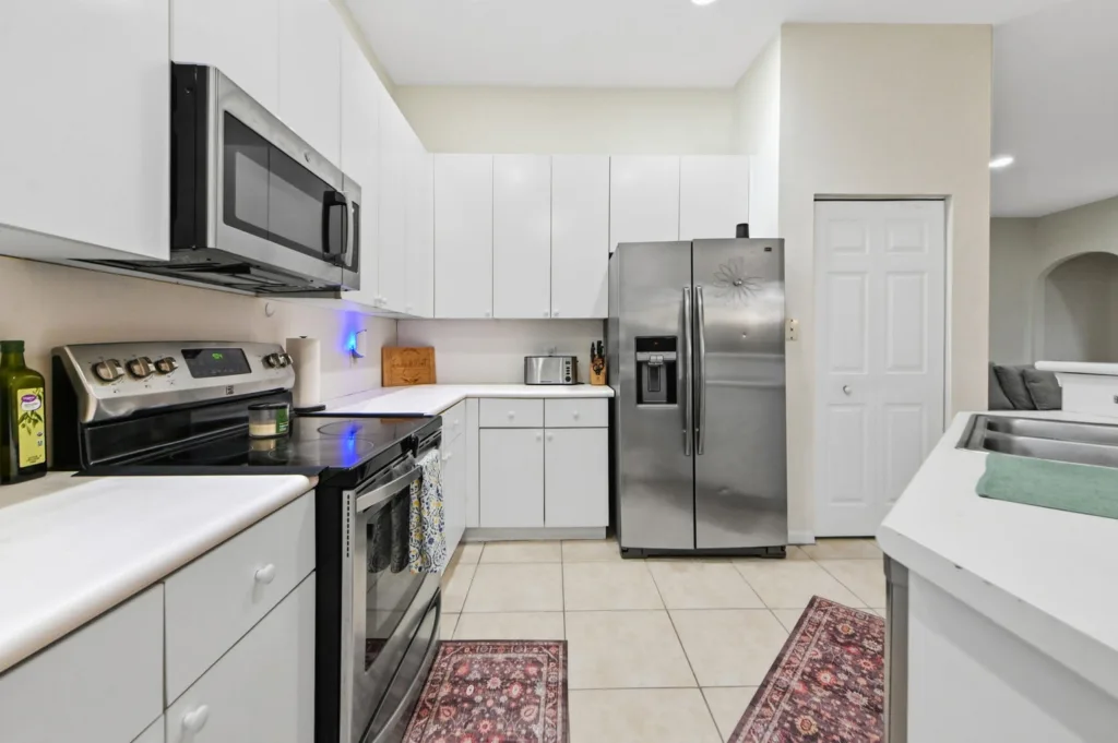 Modern white kitchen with stainless steel fridge, microwave, and stove, plus white cabinets and tiled floor.