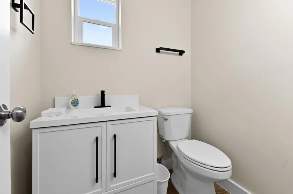 20261021192202320322000000-o - Lake Worth Homes - Lake Worth Homes Small white bathroom with a vanity sink, black faucet, and soap dispenser; toilet beside it and a towel rail on the wall above.