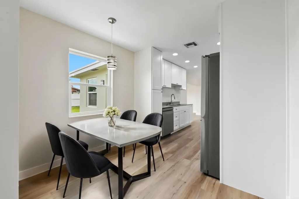 20261021192130829949000000-o - Lake Worth Homes - Lake Worth Homes Modern dining area beside a white kitchen with a marble table and four black chairs under a pendant light.