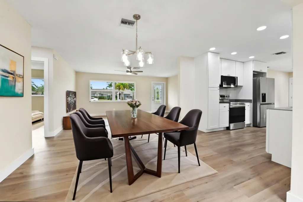 20261021192116843709000000-o - Lake Worth Homes - Lake Worth Homes Open-concept dining area with a wooden table and six dark upholstered chairs, adjacent bright kitchen.
