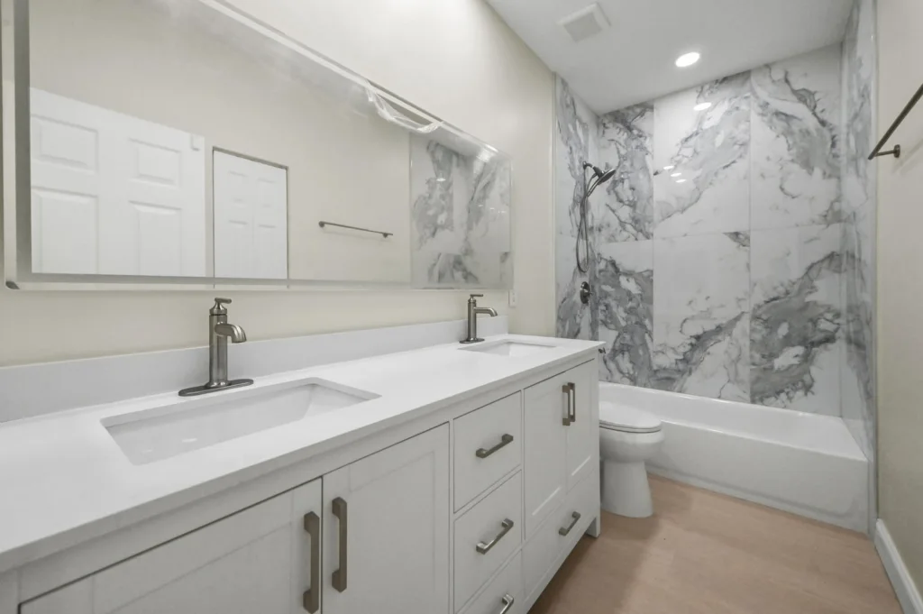 Modern bathroom featuring a white double-sink vanity, silver faucets, and a marble-tiled shower wall.