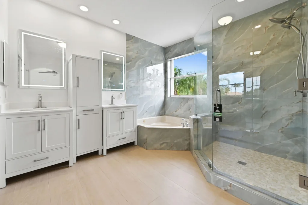 Modern bathroom with double vanities, a built-in tub, and a glass-enclosed shower on marble walls (bright, contemporary design).