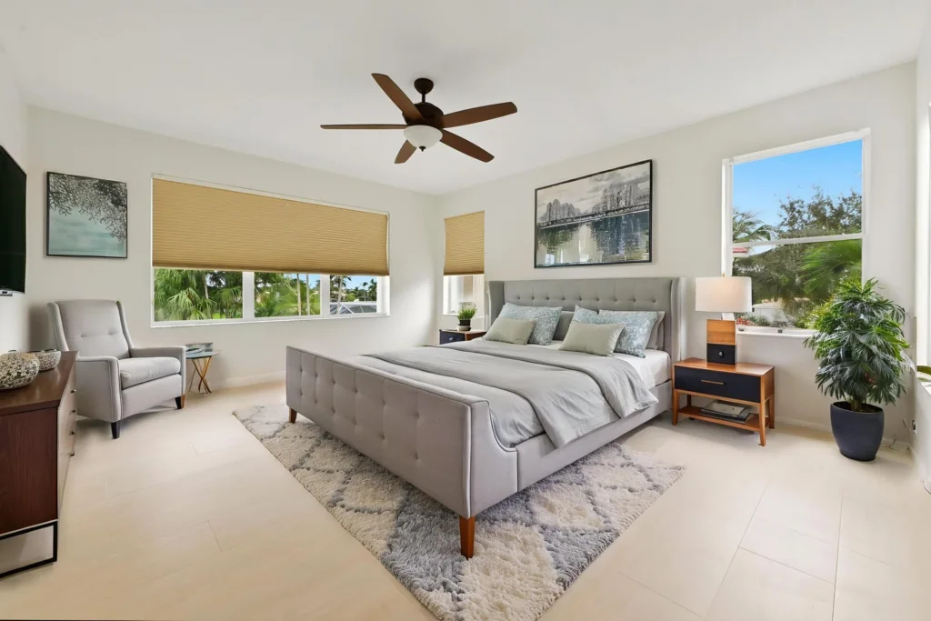 Bright, modern bedroom featuring a gray upholstered king bed with tufted headboard, two nightstands, and a ceiling fan.