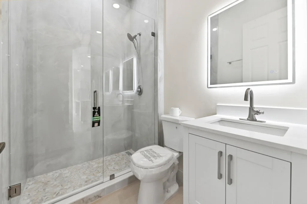 Modern bathroom with a glass-enclosed shower, white vanity, and toilet in a bright space.