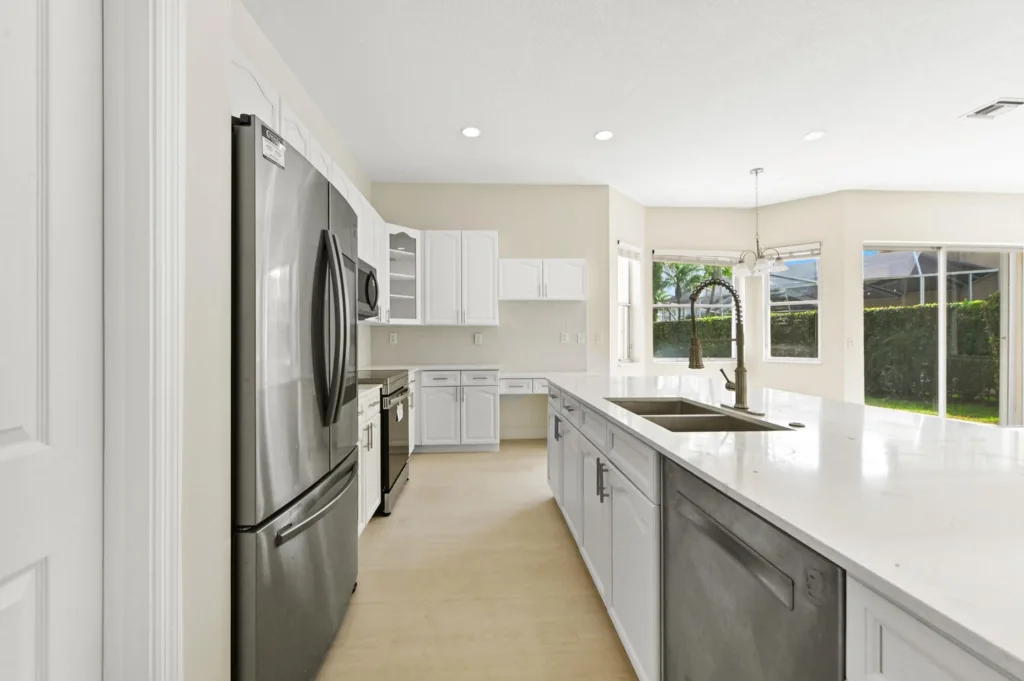 Bright, open kitchen with white cabinets, stainless steel appliances, and a large island with double sink and spring faucet.