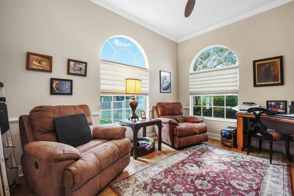 Cozy living room with two brown leather recliners, a wooden side table with a lamp, arched windows, and a red patterned rug.