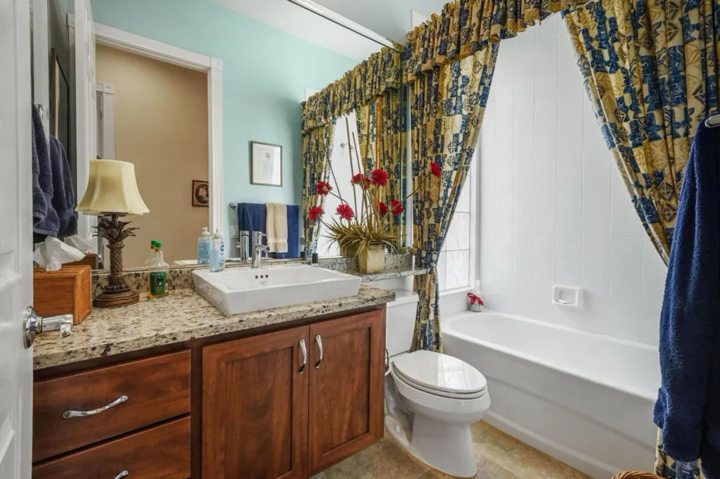 Bathroom with a granite countertop vanity, a rectangular white sink, and wooden cabinets beneath; teal walls and a floral-patterned shower curtain in the background.