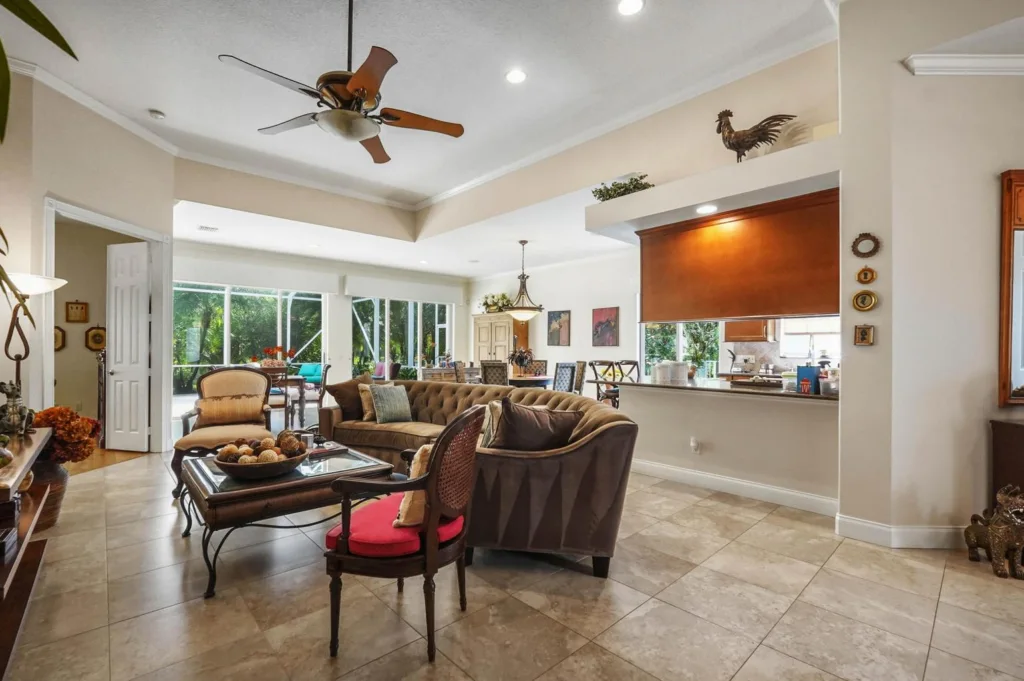 Open living room with a tufted brown sofa, beige armchairs, glass coffee table, and large windows overlooking greenery