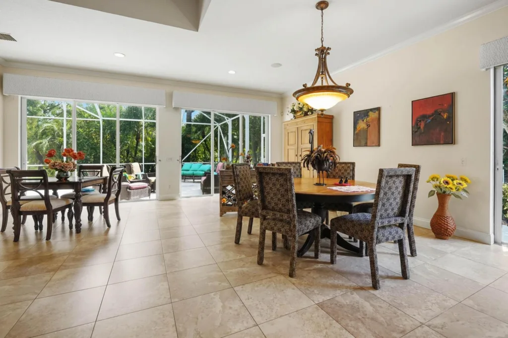 Bright dining area with a round wooden table and six patterned chairs, near large sliding glass doors to an outdoor patio with greenery outside.