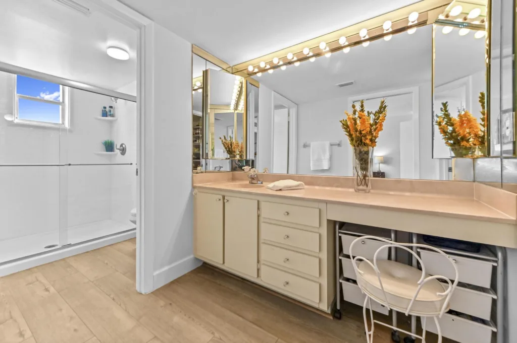20261022153954299444000000-o - Lake Worth Homes - Lake Worth Homes Bathroom vanity with peach countertop, large mirror, and globe lights; orange flowers in a vase on the counter.