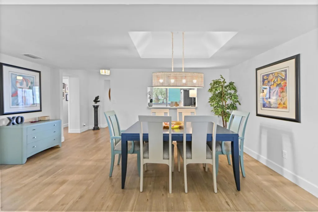 20261022153254518801000000-o - Lake Worth Homes - Lake Worth Homes Bright dining room with a blue table, white and turquoise chairs, a large woven drum chandelier, and framed art on white walls nearby.