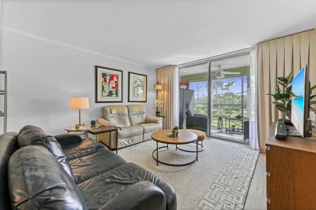 20261022153125225002000000-o - Lake Worth Homes - Lake Worth Homes Bright living room with a black leather sofa and beige loveseat facing a round wooden coffee table, sliding glass doors to a balcony in the background.