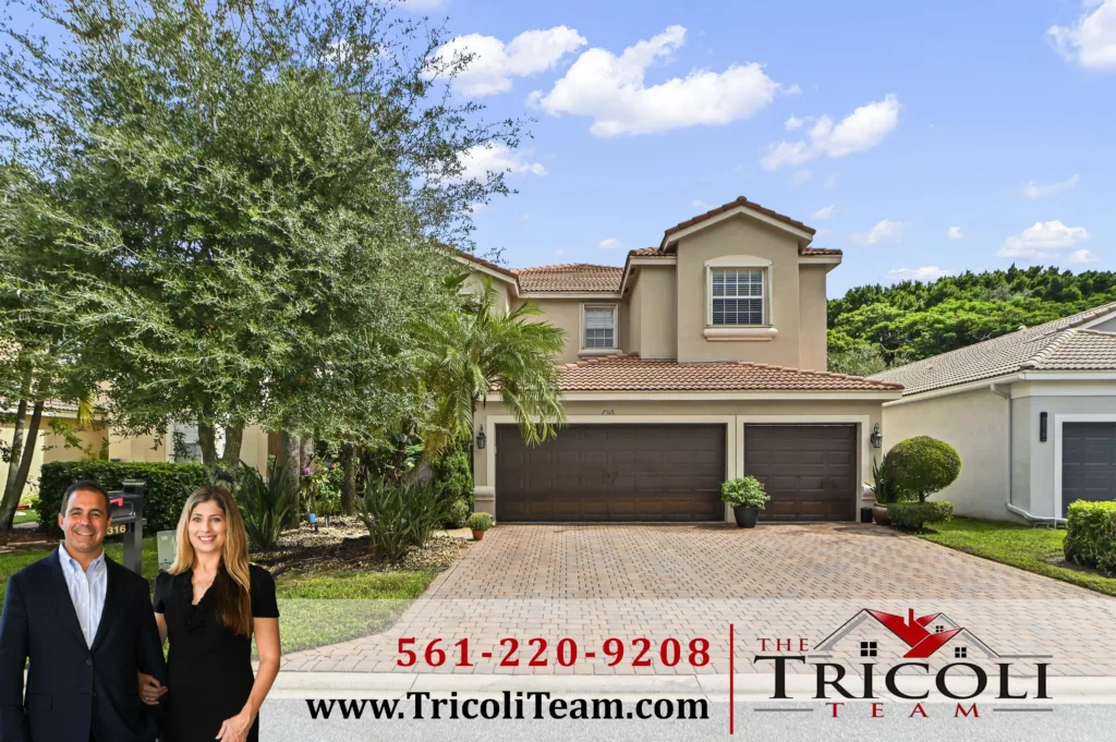 Homes for Sale in Villages of Windsor Lake Worth FL 33467 2 - Lake Worth Homes - Lake Worth Homes Two smiling real estate agents stand in front of a beige, two‑story house with a brick driveway and greenery, beside a banner reading Tricoli Team with a phone number and website.